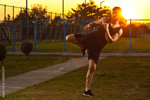 Athlete trains on a sunset background. The boxer warms up near the stadium. Contrasting dramatic shadows on the face as an artistic effect. The guy on the playground.