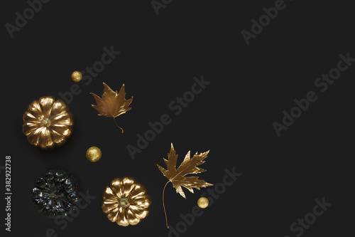 Trendy background with black and gold flying Halloween pumpkin, maple leaves on isolated on black background. Flat lay, top view, copy space.