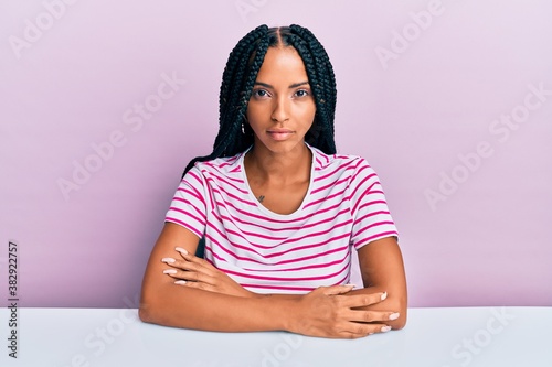Konstfotografi Beautiful hispanic woman wearing casual clothes sitting on the table with serious expression on face