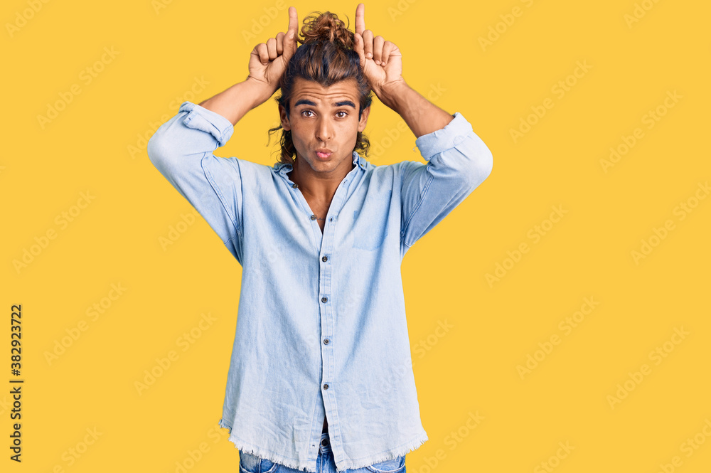 Young hispanic man wearing summer style doing funny gesture with finger over head as bull horns Young hispanic man wearing summer style doing funny gesture with finger over head as bull horns