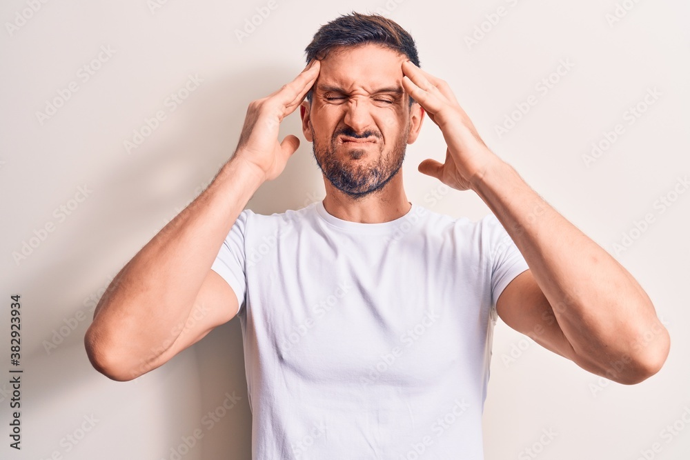 Young handsome man wearing casual t-shirt standing over isolated white background with hand on head, headache because stress. Suffering migraine. Young handsome man wearing casual t-shirt standing over isolated white background with hand on head, headache because stress. Suffering migraine.