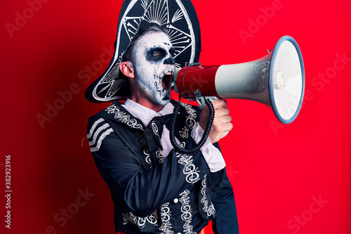 Scary man wearing day of the dead make up and costumbre from traditional ritual in Mexico shouting through megaphone