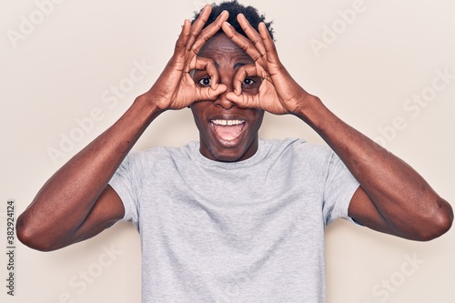 Young african american man wearing casual clothes doing ok gesture like binoculars sticking tongue out, eyes looking through fingers. crazy expression.