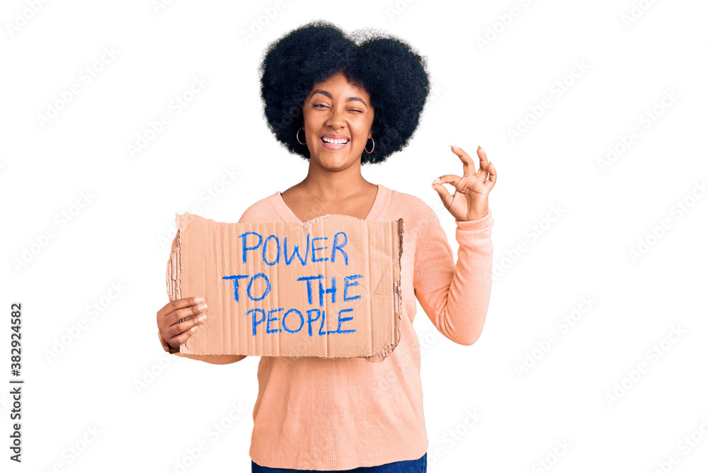 Young african american girl holding power to the people banner doing ok sign with fingers, smiling friendly gesturing excellent symbol Young african american girl holding power to the people banner doing ok sign with fingers, smiling friendly gesturing excellent symbol