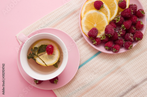 lemon wedges and raspberries in a pink plate, a cup of tea on a pink background. Flat lay of summer. Food concept
