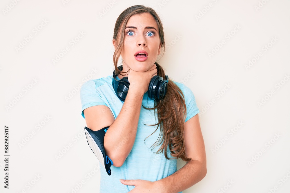 Beautiful young caucasian woman wearing gym clothes and using headphones shouting and suffocate because painful strangle. health problem. asphyxiate and suicide concept. Beautiful young caucasian woman wearing gym clothes and using headphones shouting and suffocate because painful strangle. health problem. asphyxiate and suicide concept.