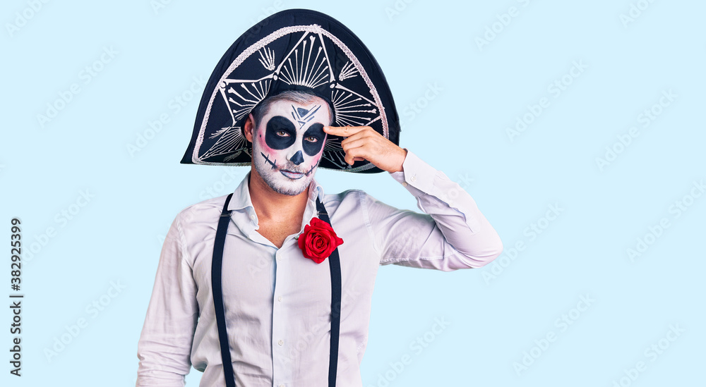 Man wearing day of the dead costume over background pointing unhappy to pimple on forehead, ugly infection of blackhead. acne and skin problem Man wearing day of the dead costume over background pointing unhappy to pimple on forehead, ugly infection of blackhead. acne and skin problem