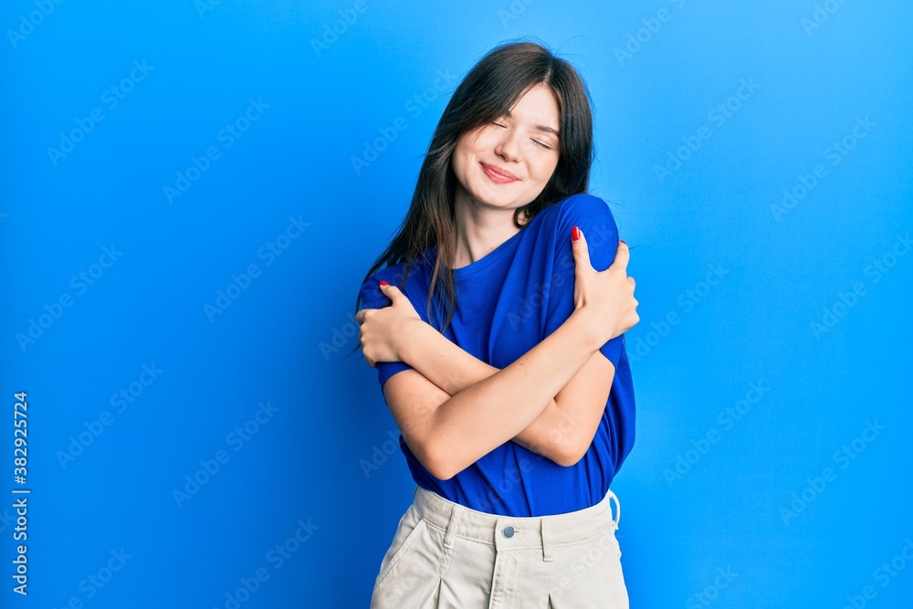 Young beautiful caucasian girl wearing casual clothes hugging oneself happy and positive, smiling confident. self love and self care Young beautiful caucasian girl wearing casual clothes hugging oneself happy and positive, smiling confident. self love and self care