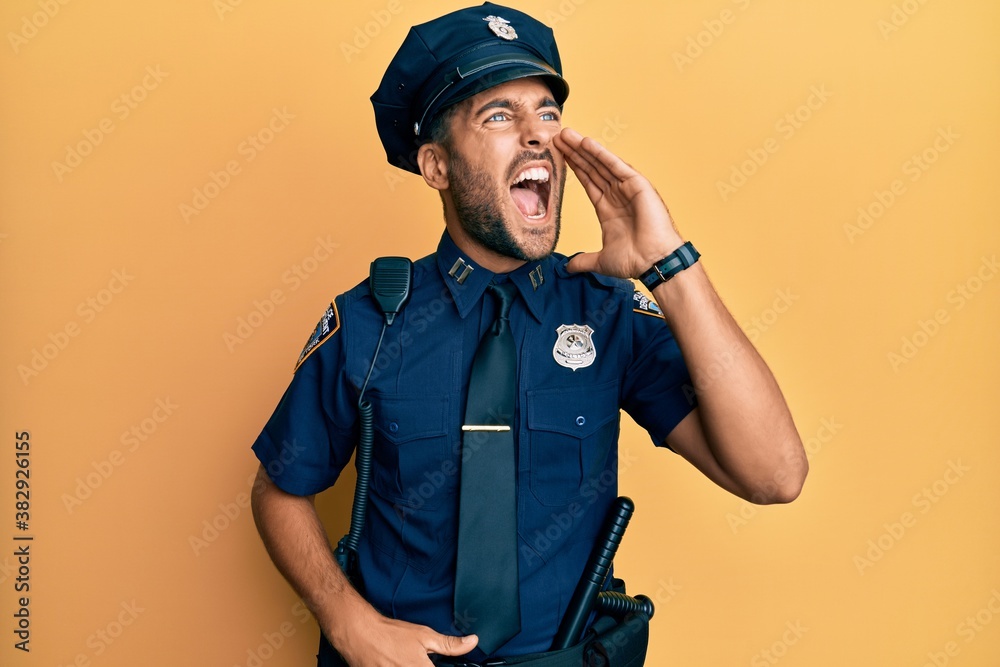 Handsome hispanic man wearing police uniform shouting and screaming loud to side with hand on mouth. communication concept. Handsome hispanic man wearing police uniform shouting and screaming loud to side with hand on mouth. communication concept.
