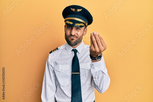 Handsome hispanic man wearing airplane pilot uniform doing italian gesture with hand and fingers confident expression © Krakenimages.com