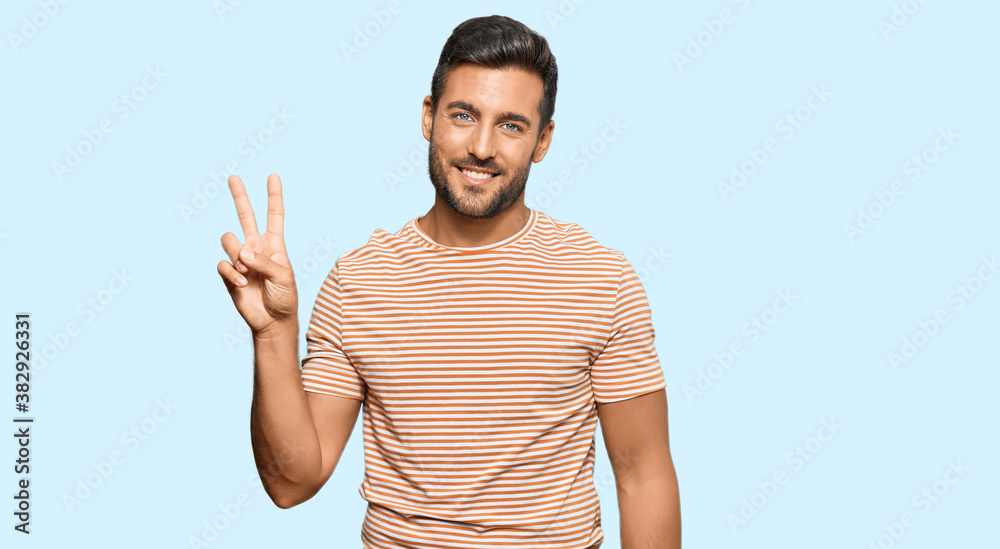 Handsome hispanic man wearing casual clothes smiling looking to the camera showing fingers doing victory sign. number two.