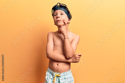 Cute blond kid wearing swimwear and swimmer glasses serious face thinking about question with hand on chin, thoughtful about confusing idea © Krakenimages.com