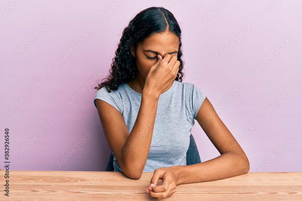 Young african american girl wearing casual clothes sitting on the table tired rubbing nose and eyes feeling fatigue and headache. stress and frustration concept. Young african american girl wearing casual clothes sitting on the table tired rubbing nose and eyes feeling fatigue and headache. stress and frustration concept.