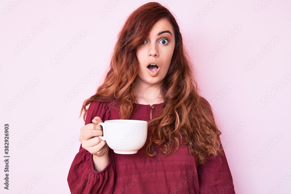 Young beautiful woman holding coffee scared and amazed with open mouth for surprise, disbelief face Young beautiful woman holding coffee scared and amazed with open mouth for surprise, disbelief face