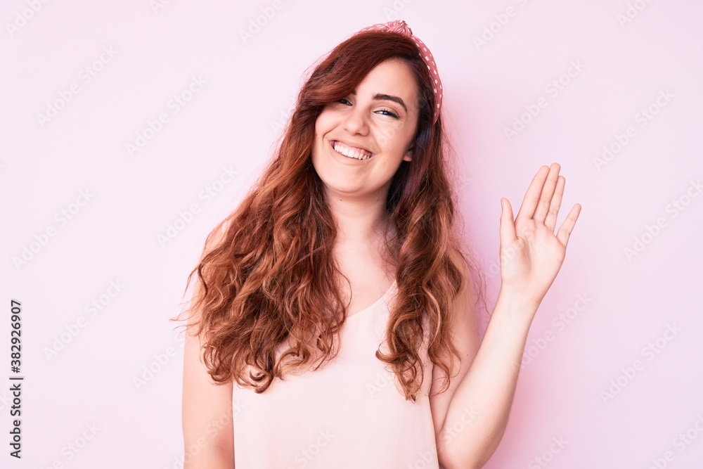 Young beautiful woman wearing casual clothes waiving saying hello happy and smiling, friendly welcome gesture Young beautiful woman wearing casual clothes waiving saying hello happy and smiling, friendly welcome gesture
