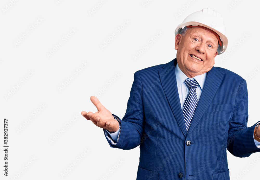 Senior handsome grey-haired man wearing suit and architect hardhat clueless and confused expression with arms and hands raised. doubt concept.