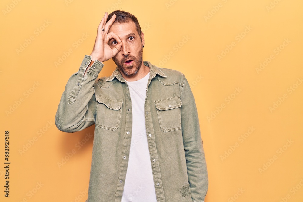 Young handsome man wearing casual clothes doing ok gesture shocked with surprised face, eye looking through fingers. unbelieving expression.