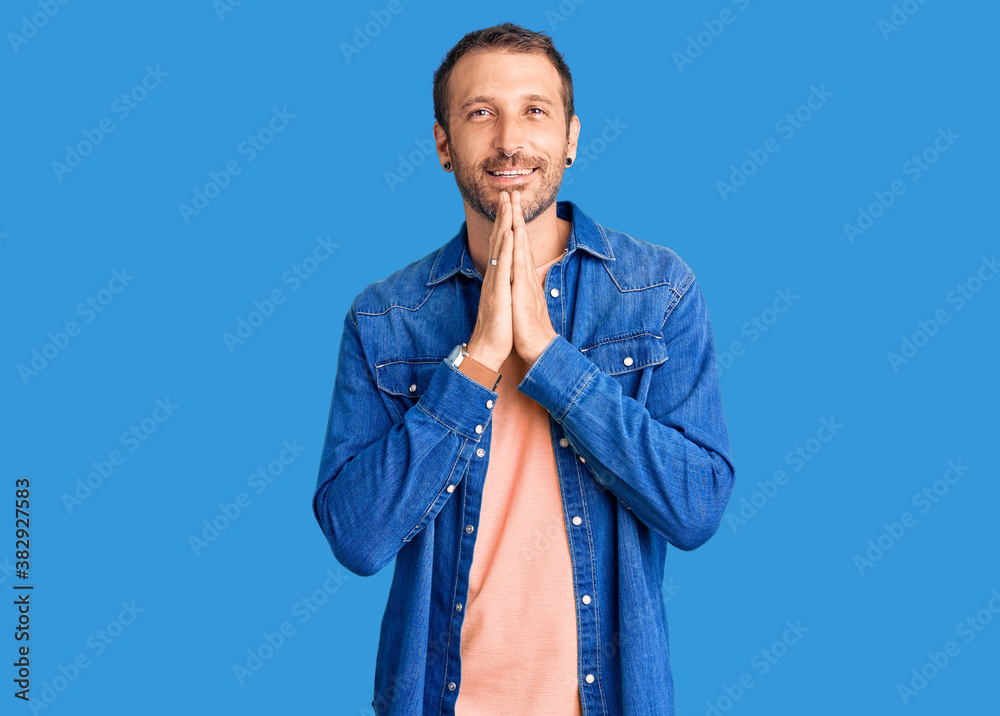 Young handsome man wearing casual clothes praying with hands together asking for forgiveness smiling confident. Young handsome man wearing casual clothes praying with hands together asking for forgiveness smiling confident.