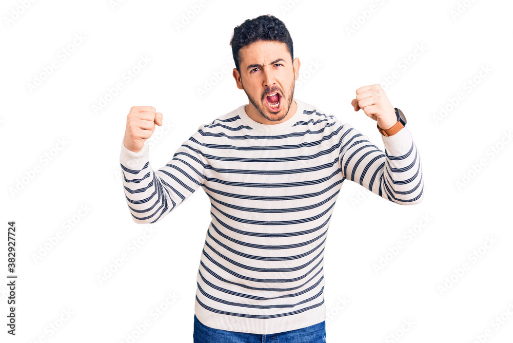 Young hispanic man wearing casual clothes angry and mad raising fists frustrated and furious while shouting with anger. rage and aggressive concept. Young hispanic man wearing casual clothes angry and mad raising fists frustrated and furious while shouting with anger. rage and aggressive concept.