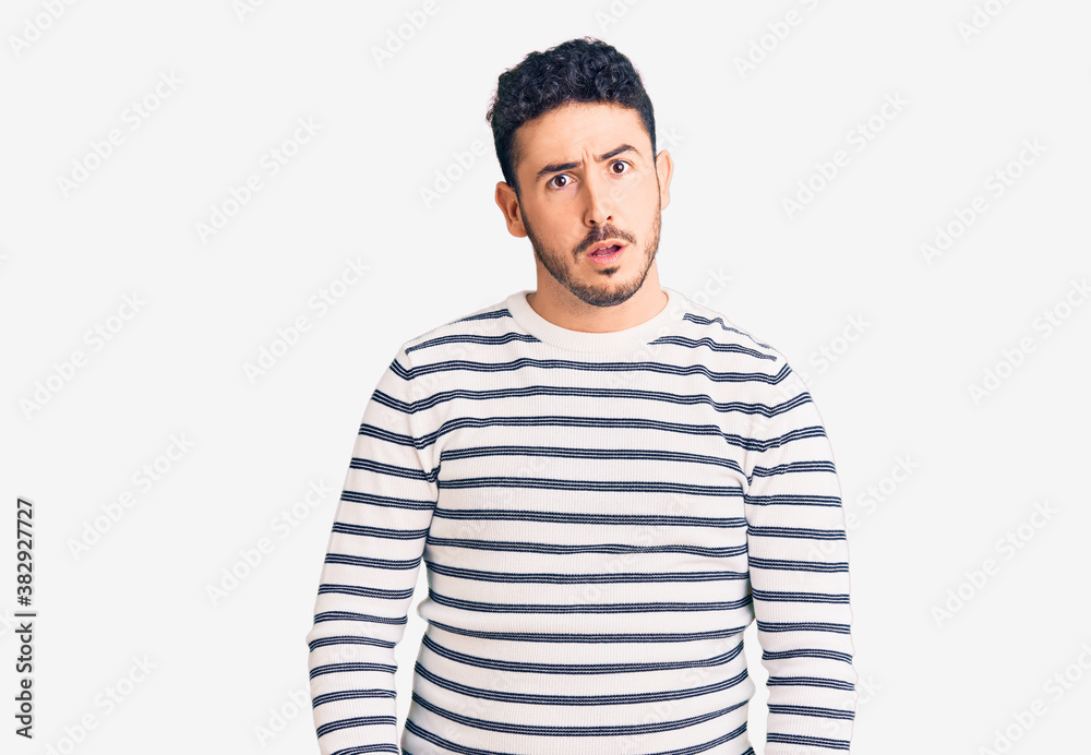 Young hispanic man wearing casual clothes in shock face, looking skeptical and sarcastic, surprised with open mouth