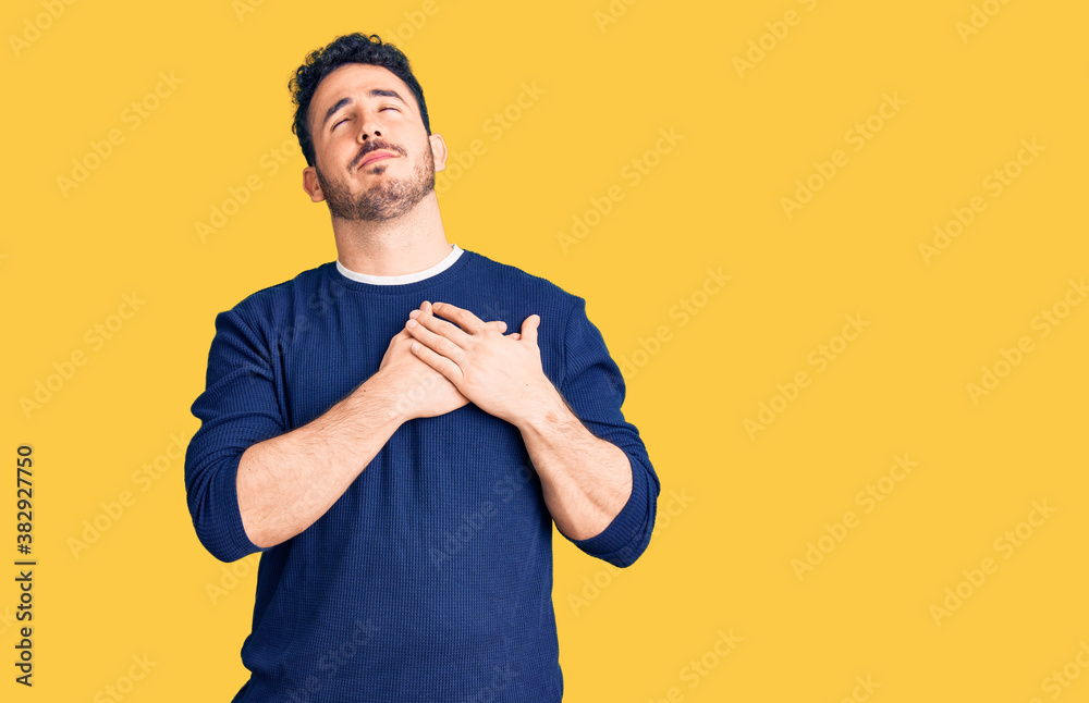 Young hispanic man wearing casual clothes smiling with hands on chest with closed eyes and grateful gesture on face. health concept. Young hispanic man wearing casual clothes smiling with hands on chest with closed eyes and grateful gesture on face. health concept.