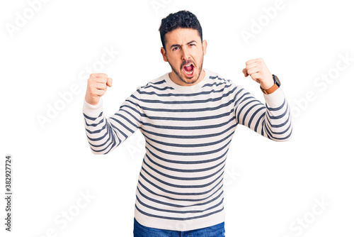 Young hispanic man wearing casual clothes angry and mad raising fists frustrated and furious while shouting with anger. rage and aggressive concept.