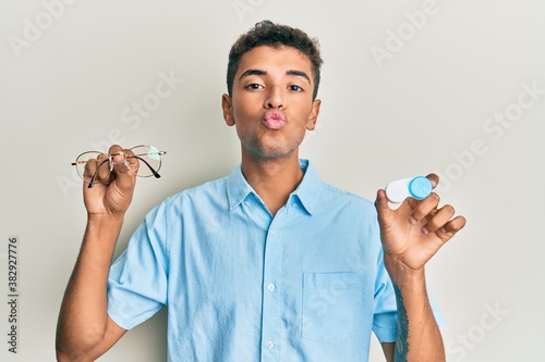 Young handsome african american man holding glasses and contact lenses looking at the camera blowing a kiss being lovely and sexy. love expression.