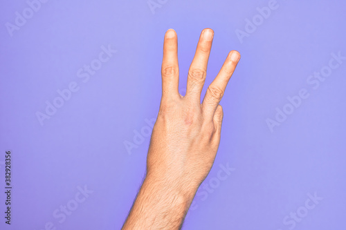 Hand of caucasian young man showing fingers over isolated purple background counting number 3 showing three fingers