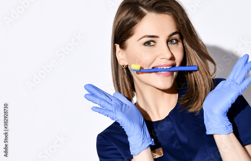 Portrait of young smiling woman doctor dentist in dark blue uniform and gloves with professional toothbrush in mouth