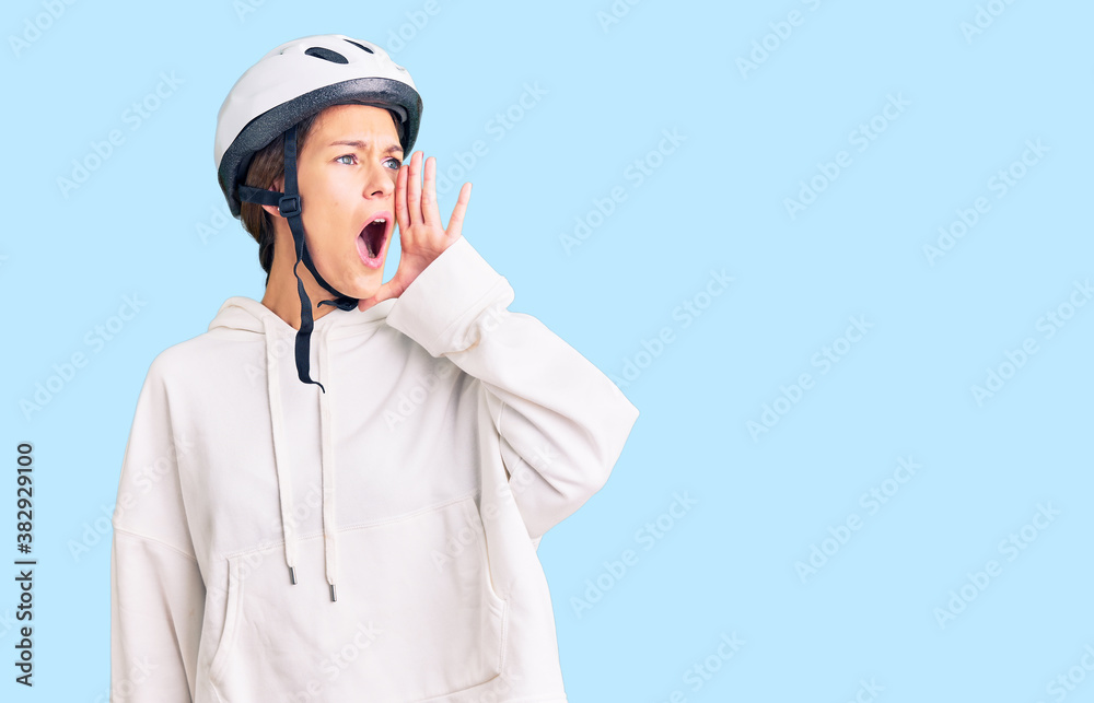 Beautiful brunette young woman wearing bike helmet and sporty clothes shouting and screaming loud to side with hand on mouth. communication concept. Beautiful brunette young woman wearing bike helmet and sporty clothes shouting and screaming loud to side with hand on mouth. communication concept.