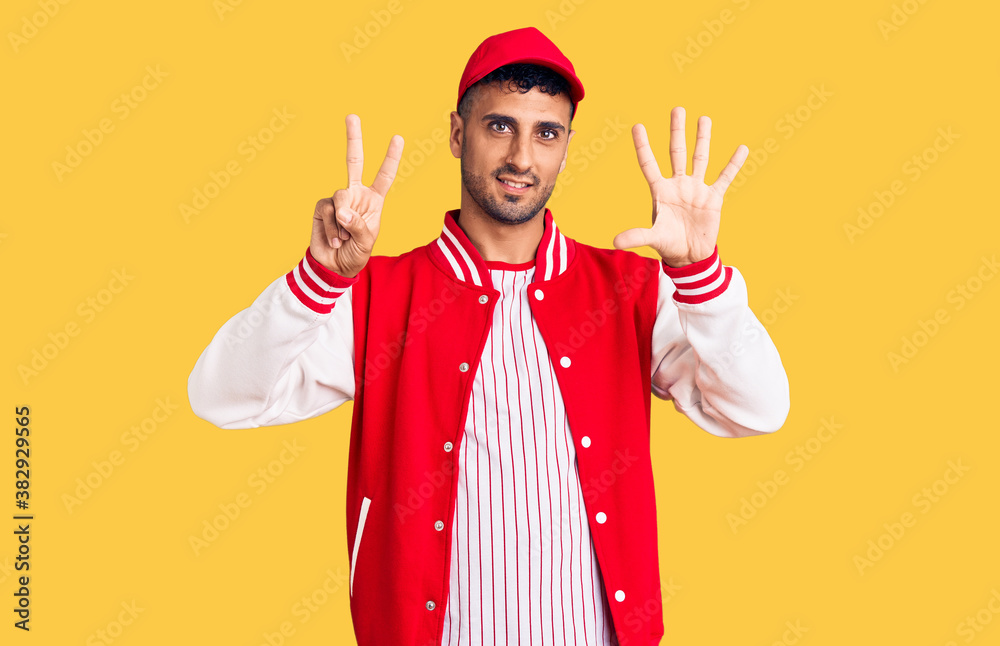 Young hispanic man wearing baseball uniform showing and pointing up with fingers number seven while smiling confident and happy. Young hispanic man wearing baseball uniform showing and pointing up with fingers number seven while smiling confident and happy.