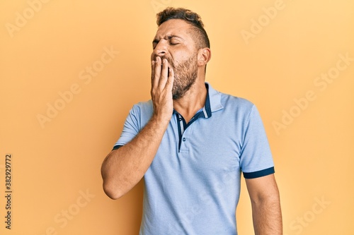 Handsome man with beard wearing casual clothes bored yawning tired covering mouth with hand. restless and sleepiness. © Krakenimages.com