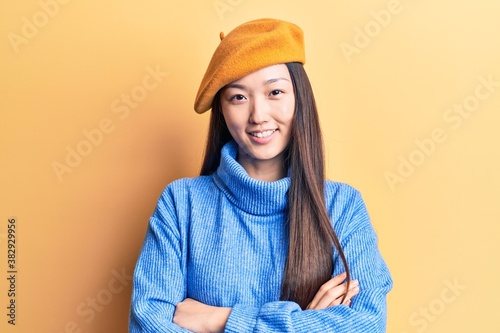 Young beautiful chinese woman wearing turtleneck sweater and french beret happy face smiling with crossed arms looking at the camera. positive person.
