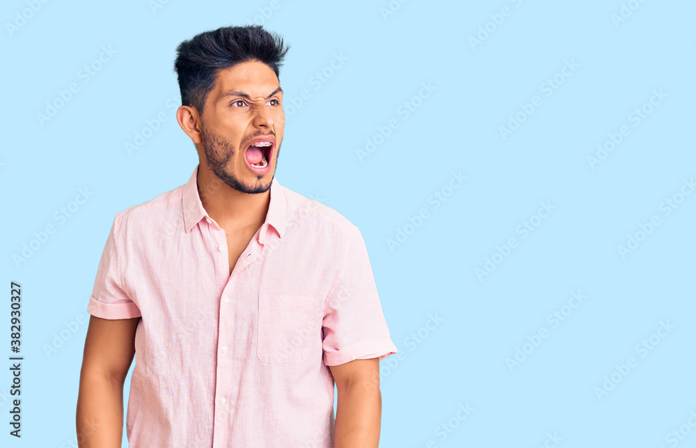 Handsome latin american young man wearing casual summer shirt angry and mad screaming frustrated and furious, shouting with anger. rage and aggressive concept. Handsome latin american young man wearing casual summer shirt angry and mad screaming frustrated and furious, shouting with anger. rage and aggressive concept.