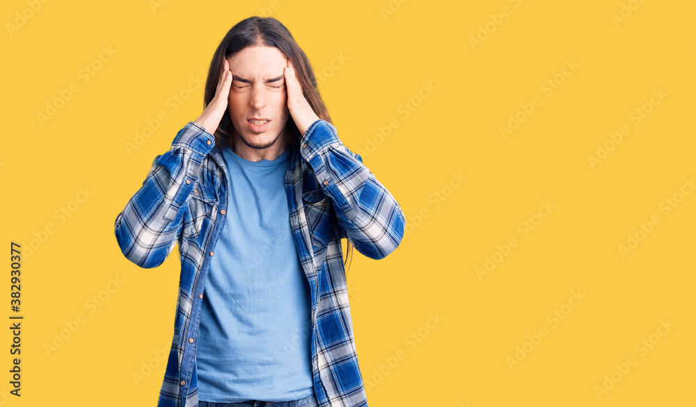 Young adult man with long hair wearing casual shirt with hand on head for pain in head because stress. suffering migraine. Young adult man with long hair wearing casual shirt with hand on head for pain in head because stress. suffering migraine.