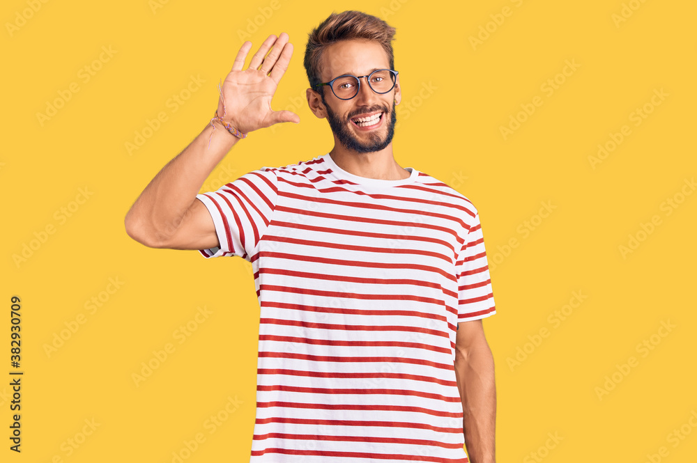 Handsome blond man with beard wearing casual clothes and glasses waiving saying hello happy and smiling, friendly welcome gesture Handsome blond man with beard wearing casual clothes and glasses waiving saying hello happy and smiling, friendly welcome gesture