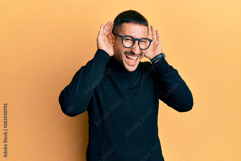Handsome man with tattoos wearing turtleneck sweater and glasses trying to hear both hands on ear gesture, curious for gossip. hearing problem, deaf Handsome man with tattoos wearing turtleneck sweater and glasses trying to hear both hands on ear gesture, curious for gossip. hearing problem, deaf