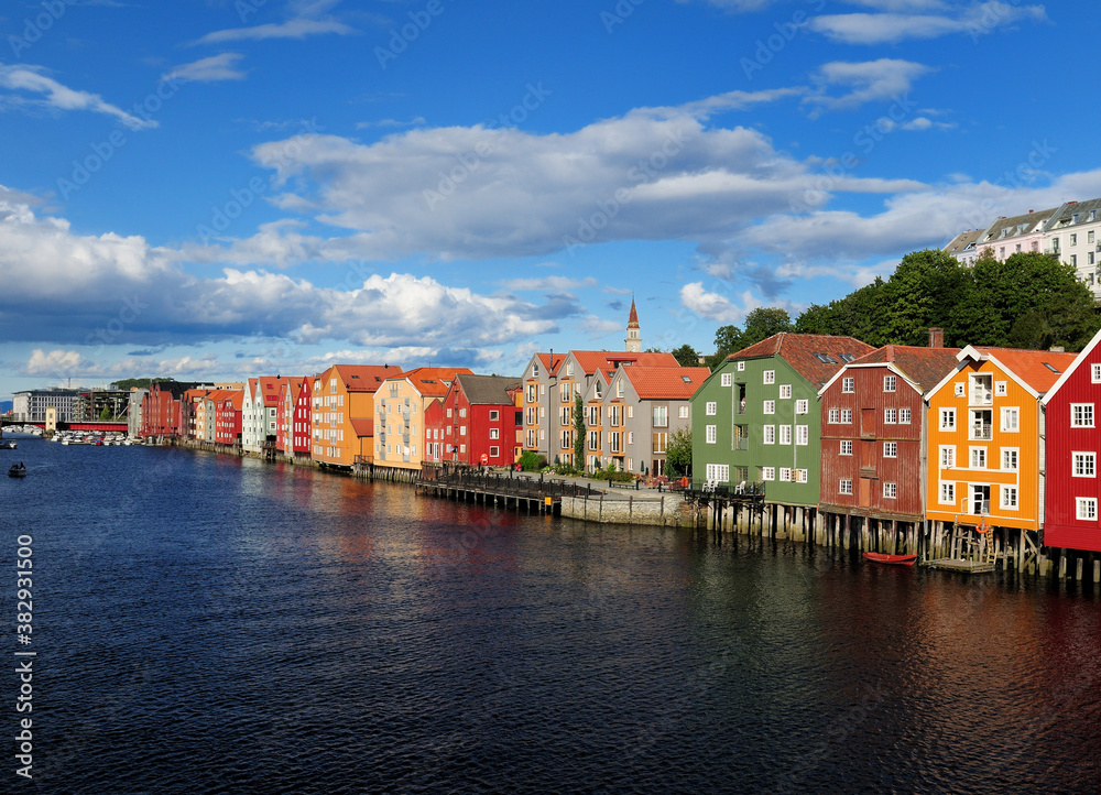 Naklejka premium View From Gamle Bybru Bridge To The Coloured Wooden Waterfront Of Bakklandet In Trondheim At The Nidelv River On A Sunny Summer Day With A Clear Blue Sky And A Few Clouds