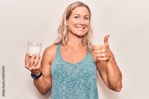 Middle age caucasian blonde woman holding a glass of milk smiling happy and positive, thumb up doing excellent and approval sign © Krakenimages.com