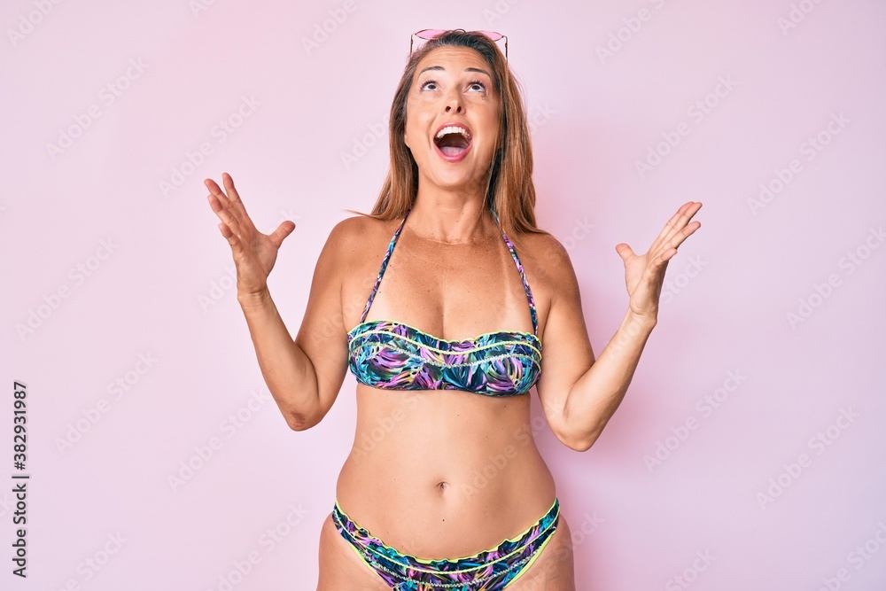 Naklejka premium Middle age hispanic woman wearing bikini crazy and mad shouting and yelling with aggressive expression and arms raised. frustration concept.