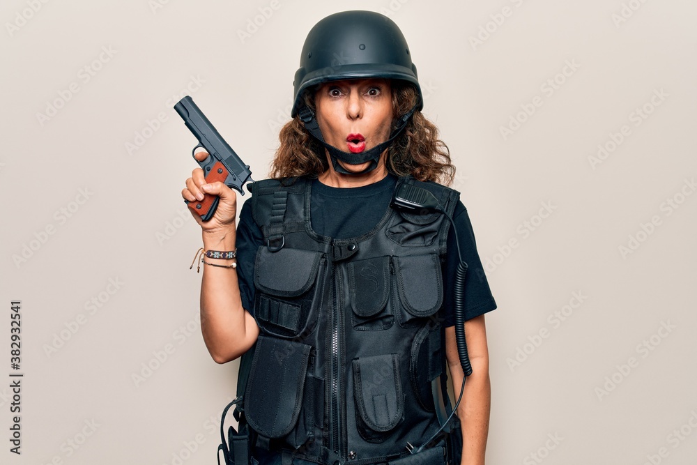 Middle age soldier woman wearing bulletproof uniform and security helmet holding gun scared and amazed with open mouth for surprise, disbelief face Middle age soldier woman wearing bulletproof uniform and security helmet holding gun scared and amazed with open mouth for surprise, disbelief face