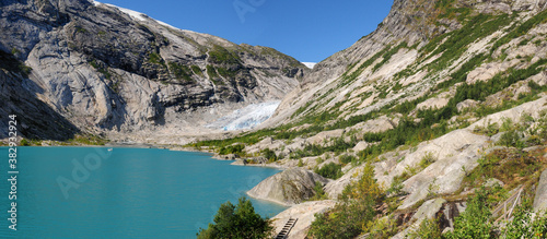 Fototapeta Naklejka Na Ścianę i Meble -  Panorama View From The Lake Nigardsbrevatnet To The Glacier Nigardsbreen In Jostedalsbreen National Park On A Sunny Summer Day With A Clear Blue Sky