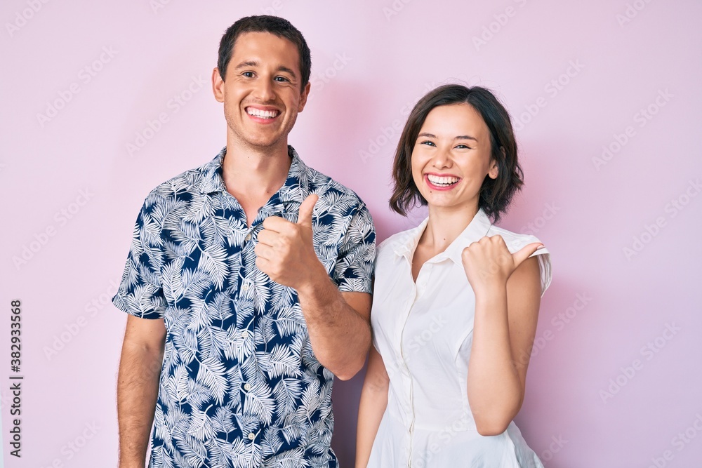 Beautiful couple wearing casual clothes pointing to the back behind with hand and thumbs up, smiling confident Beautiful couple wearing casual clothes pointing to the back behind with hand and thumbs up, smiling confident