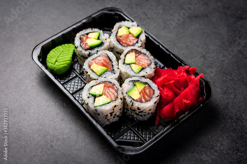 Delivery of Japanese traditional food. Salmon and avocado rolls with black and white sesame seeds in a plastic container