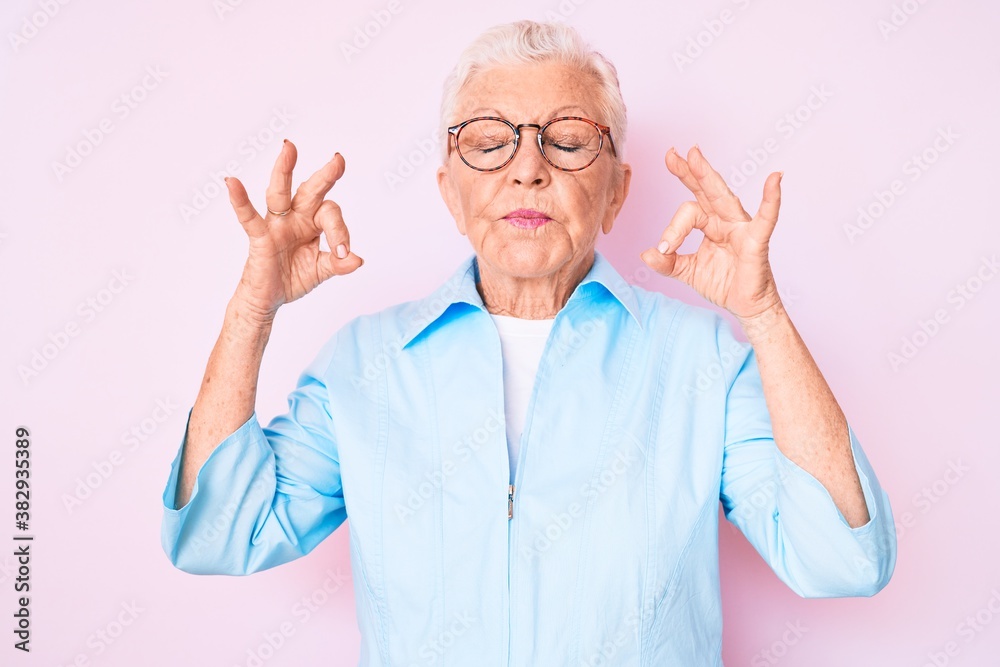 Senior beautiful woman with blue eyes and grey hair wearing glasses relax and smiling with eyes closed doing meditation gesture with fingers. yoga concept. Senior beautiful woman with blue eyes and grey hair wearing glasses relax and smiling with eyes closed doing meditation gesture with fingers. yoga concept.