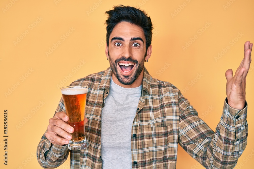 Handsome hispanic man with beard drinking a pint of beer screaming proud, celebrating victory and success very excited with raised arms Handsome hispanic man with beard drinking a pint of beer screaming proud, celebrating victory and success very excited with raised arms