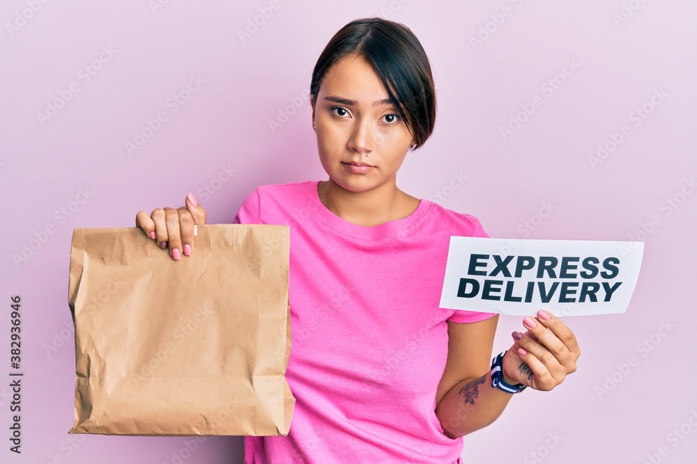 Beautiful young woman with short hair holding paper pag with express delivery text skeptic and nervous, frowning upset because of problem. negative person. Beautiful young woman with short hair holding paper pag with express delivery text skeptic and nervous, frowning upset because of problem. negative person.