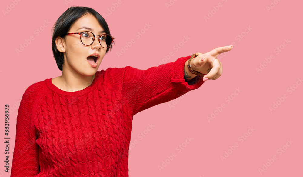 Young beautiful hispanic woman with short hair wearing casual sweater and glasses pointing with finger surprised ahead, open mouth amazed expression, something on the front Young beautiful hispanic woman with short hair wearing casual sweater and glasses pointing with finger surprised ahead, open mouth amazed expression, something on the front