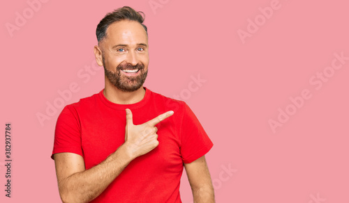 Handsome middle age man wearing casual red tshirt cheerful with a smile of face pointing with hand and finger up to the side with happy and natural expression on face