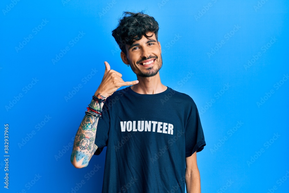 Young hispanic man wearing volunteer t shirt smiling doing phone gesture with hand and fingers like talking on the telephone. communicating concepts. Young hispanic man wearing volunteer t shirt smiling doing phone gesture with hand and fingers like talking on the telephone. communicating concepts.